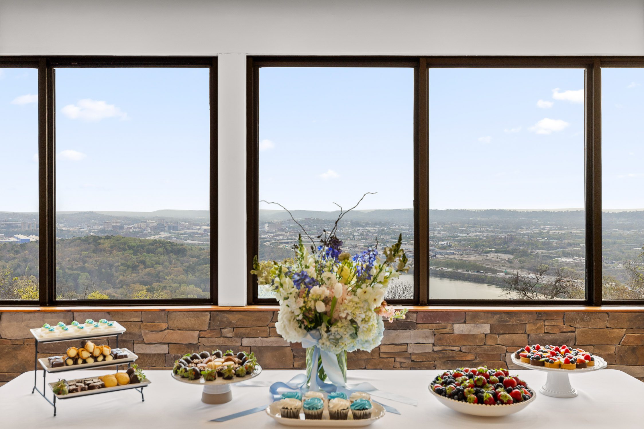 Table with desserts and flowers is set in front of windows with a view of the Tennessee River at Skyline Loft