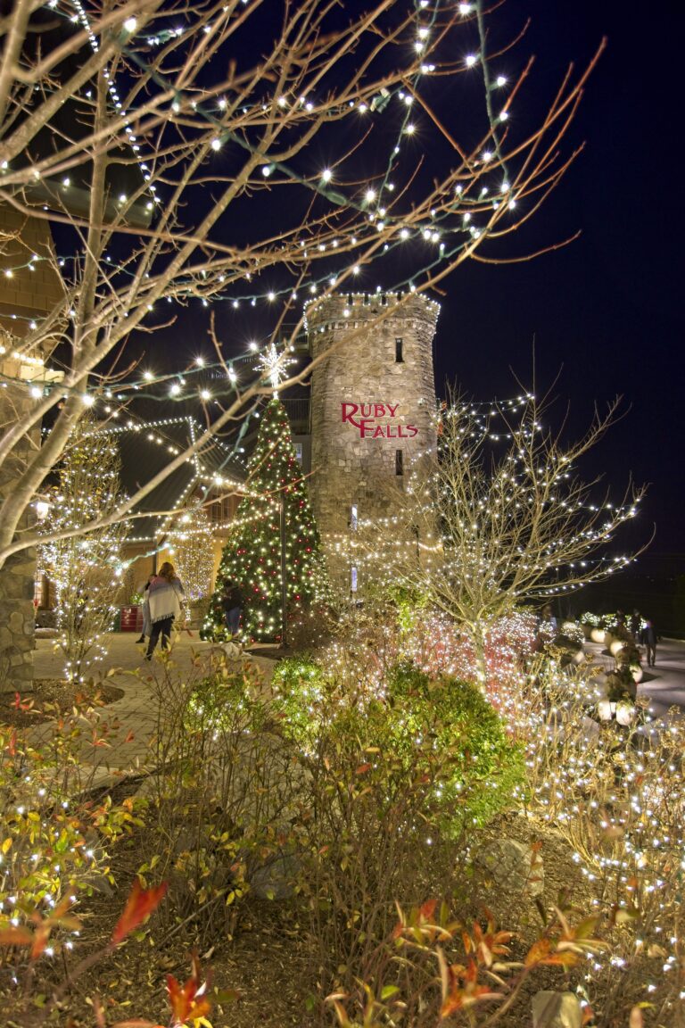 Christmas lights adorn the landscaping around the outdoor plaza at Ruby Falls with Lookout Mountain Tower made of limestone in the background.