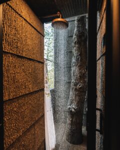 An outdoor shower with a brass rain head in luxury treehouse lodging. 