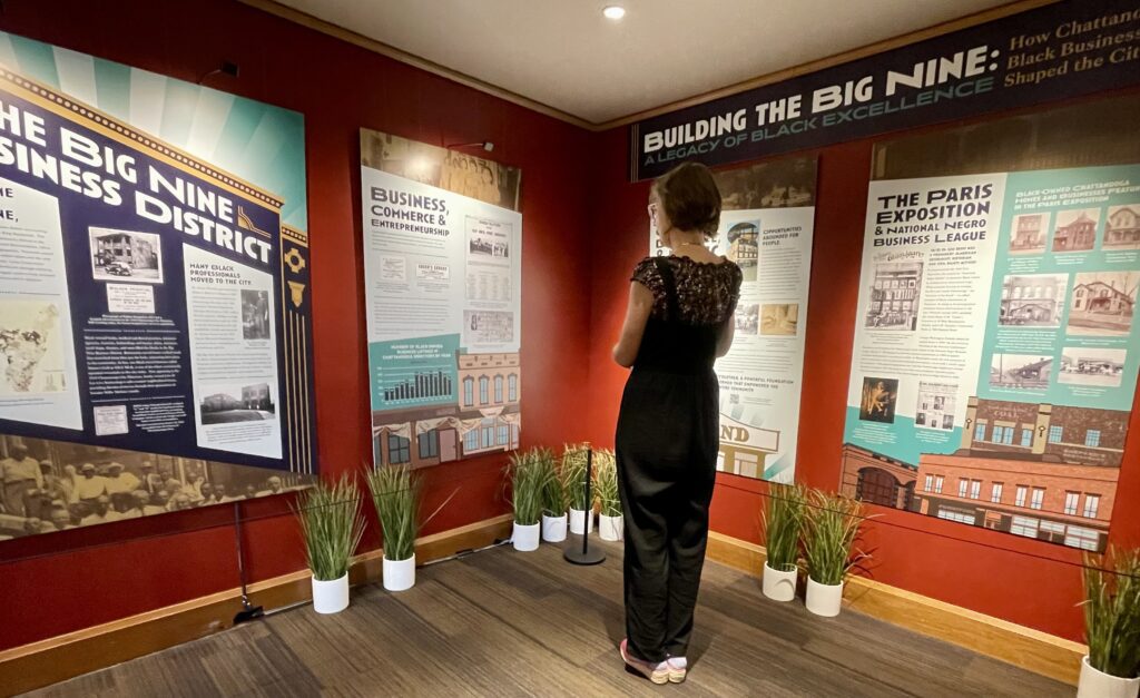 A woman wearing dark pants and a short sleeve shirt stands in a Black history exhibit at Ruby Falls, quietly reading about the Black men and women who created a thriving Black business district in Chattanooga during the Jim Crow era.