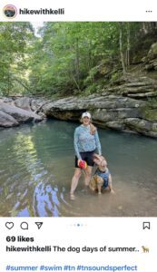 Woman stands with dog in the water at a natural swimming hole surrounded by large boulders and trees outside of Chattanooga Tennessee. 