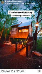 Evening view of treehouse with Ruby Falls painted on on the exterior. Cafe lights hang from the trees and light fills the windows.