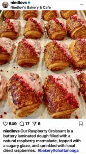 Fresh croissants filled and topped with fresh raspberries on a baking sheet at a bakery.