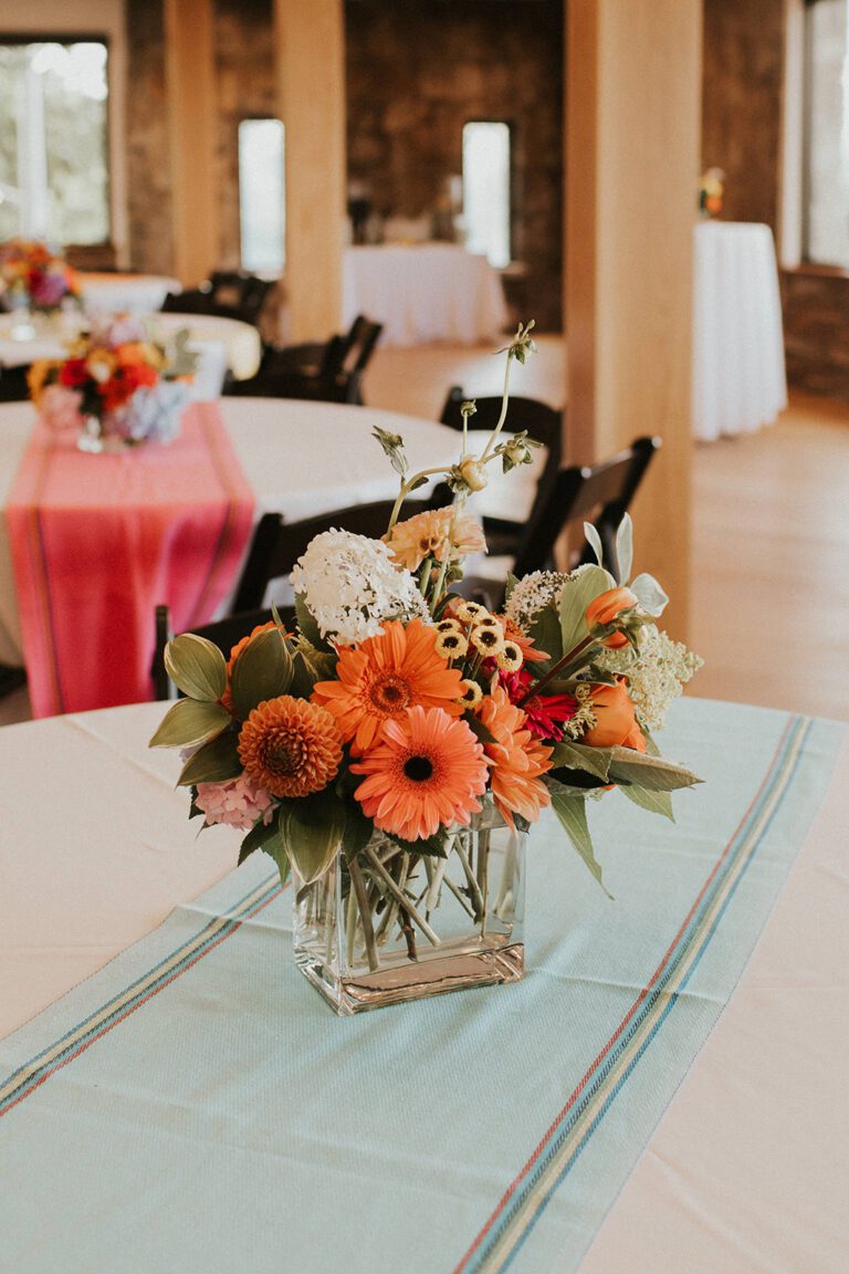 bright orange and yellow flowers in a vase set on a table at a party.