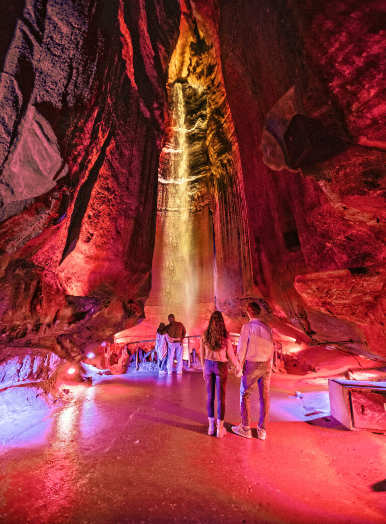 Two couples stand at a distance from each other in front of the waterfall inside Ruby Falls Cave.