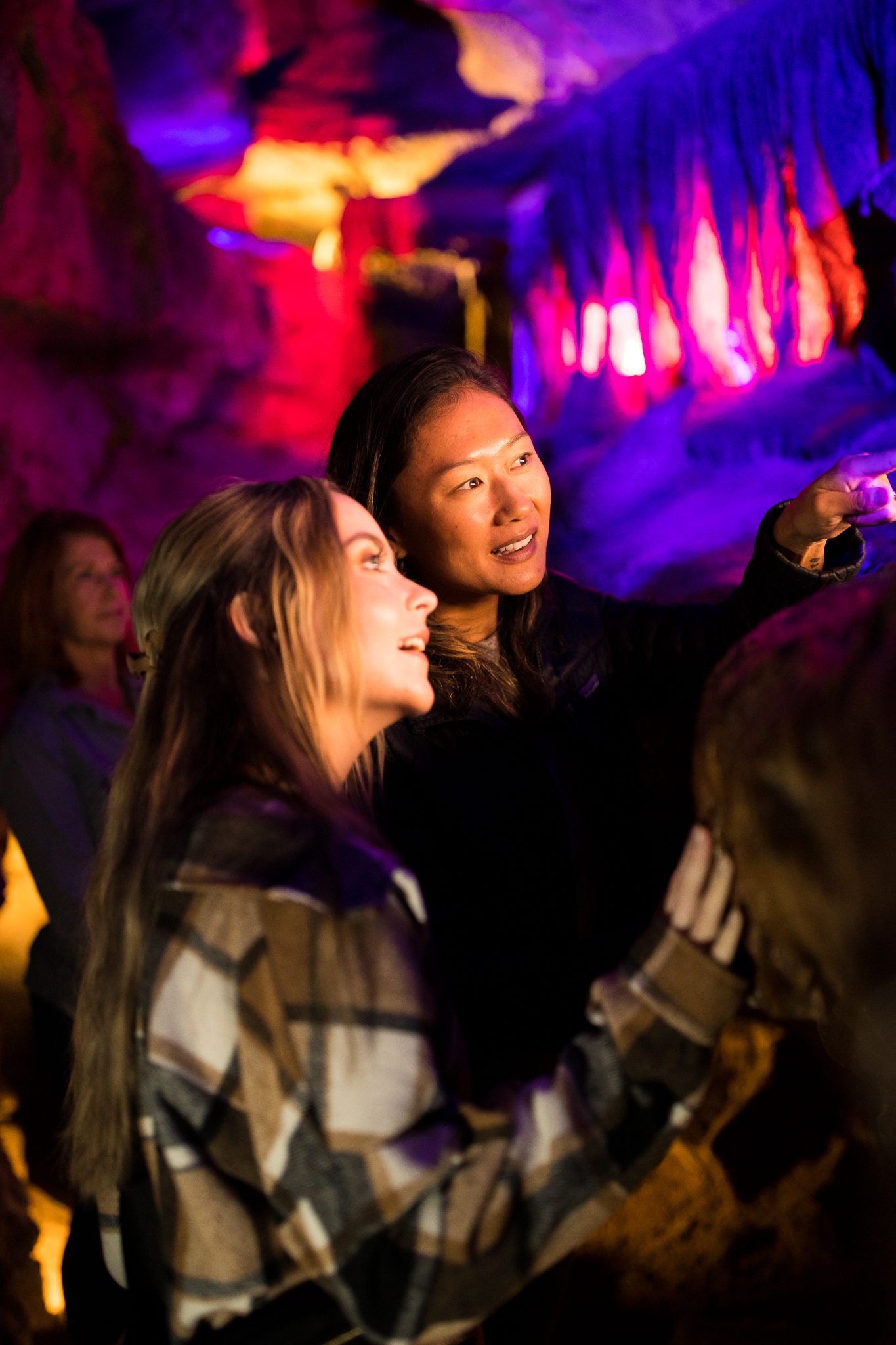 Two women stand against a rock formation looking deeper into the caves. The woman in the back points to the off-camera point of interest.