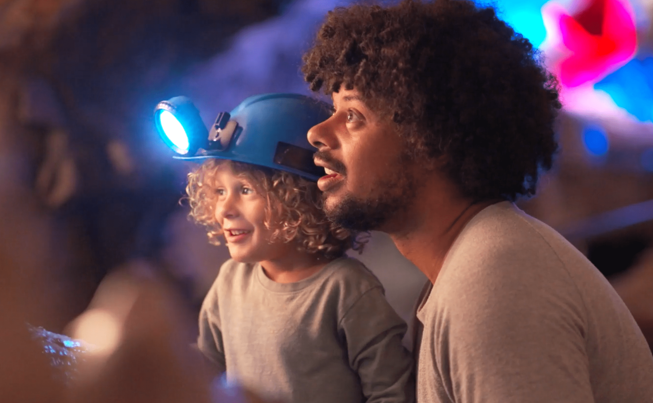 A man, with a child wearing a lighted helmet, look at cave formations